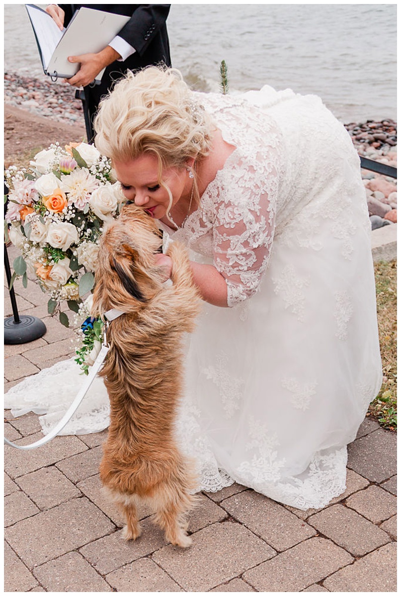happy bride bends down to get the rings and give the furry ring bearer a smooch during this custom-crafted ceremony