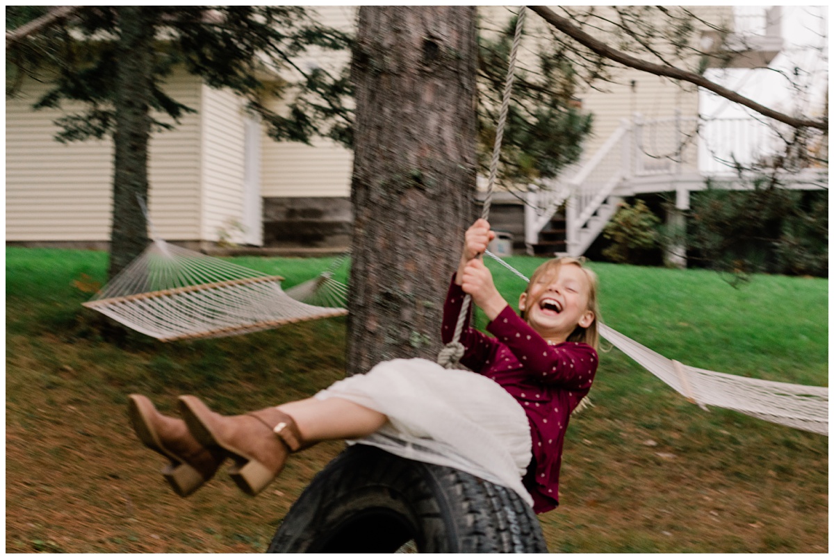 little blonde girl in a white dress and fuschia sweater laughs on a tire swing with comfort and cashmere photography
