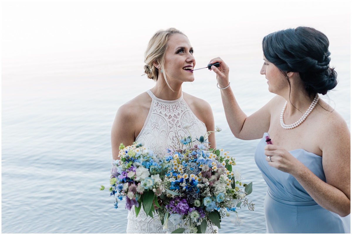 A bridesmaid helps the bride refresh her lipstick during wedding photos