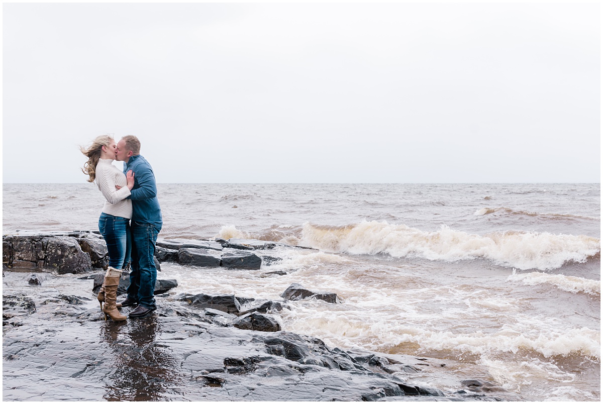 Couple kisses on the shore of Lake Superior during an engagement session with Comfort & Cashmere images