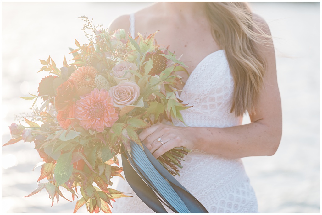 bride holds gorgeous bouquet full of seasonal summer flowers with a lake shining in the background. Image by Comfort and Cashmere