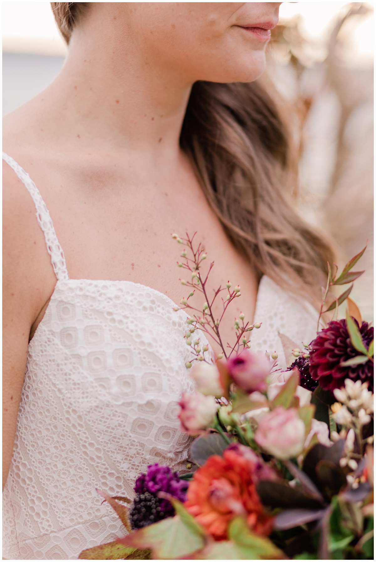 close up of a bride's chin and a spaghetti strapped, lacey gown, accented by a beautiful pop of color with zinnias and other exotic flowers