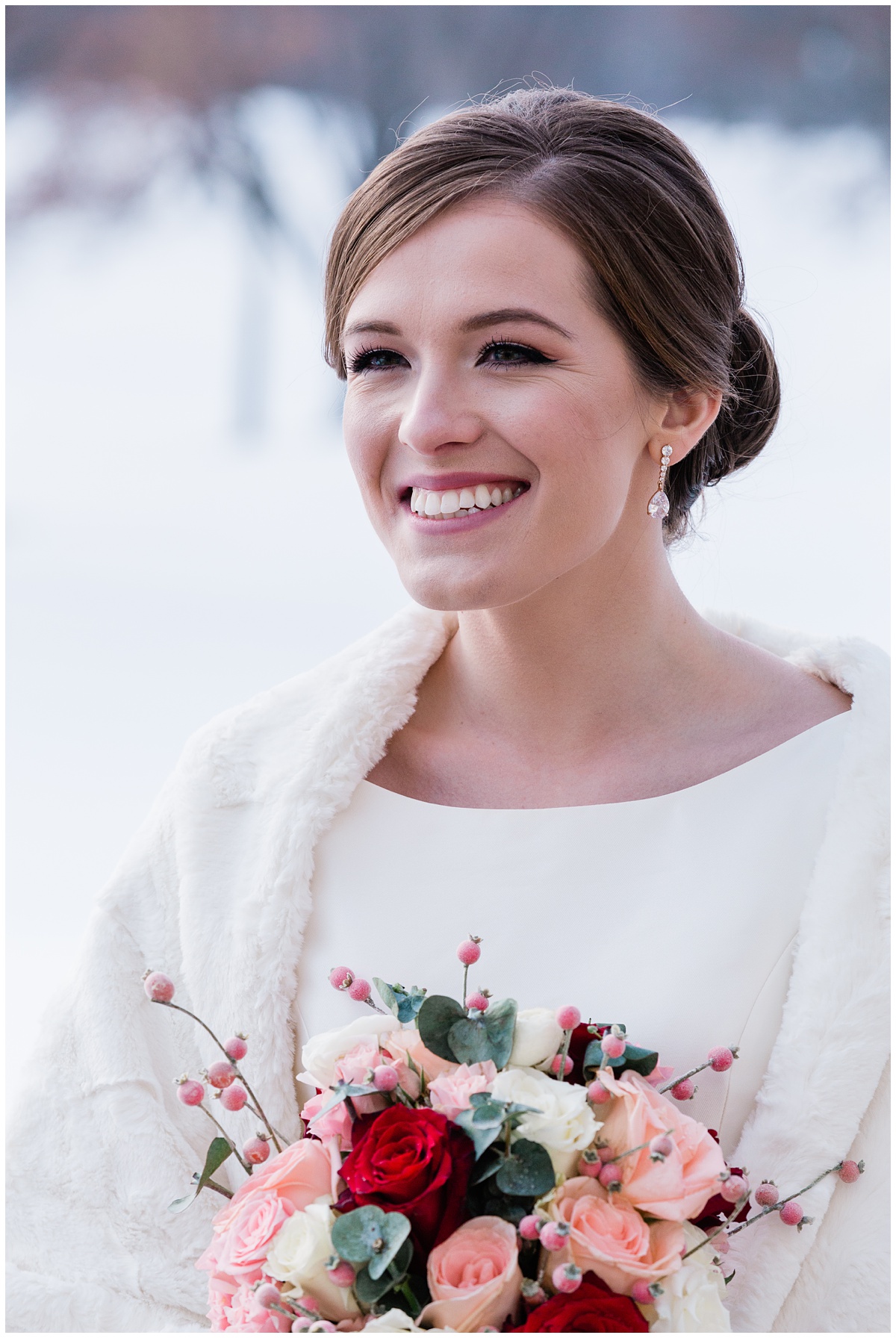 timeless and beautiful winter bride smiles over at her groom while outside with snow in the background and a pop of pinks and reds and eucalyptus in her bouquet. Comfort and Cashmere images.