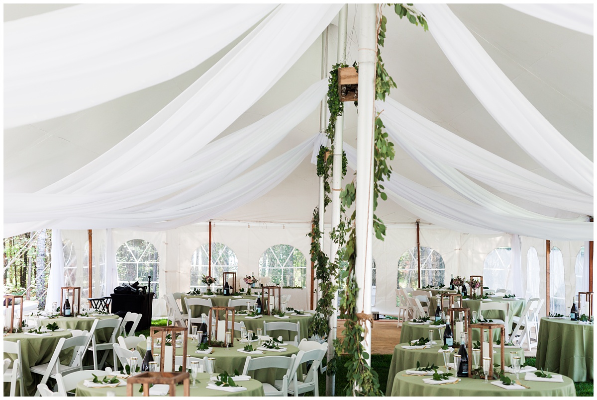 Inside of a large white reception tent, decorated for a wedding with green linens and florals.