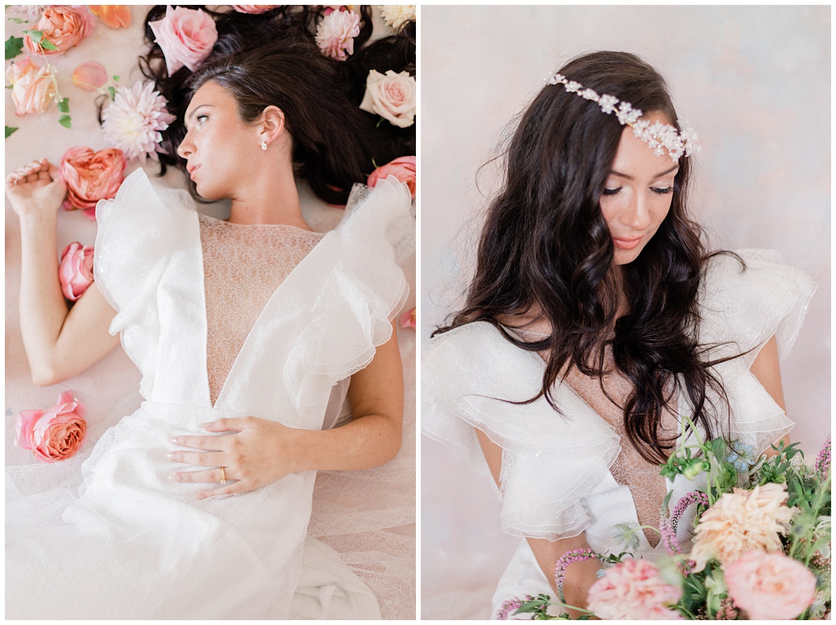 Beautiful brunette bride wearing a dress with flowing short sleeves lays in bed of flowers and then looks down at her bouquet wearing a headpiece
