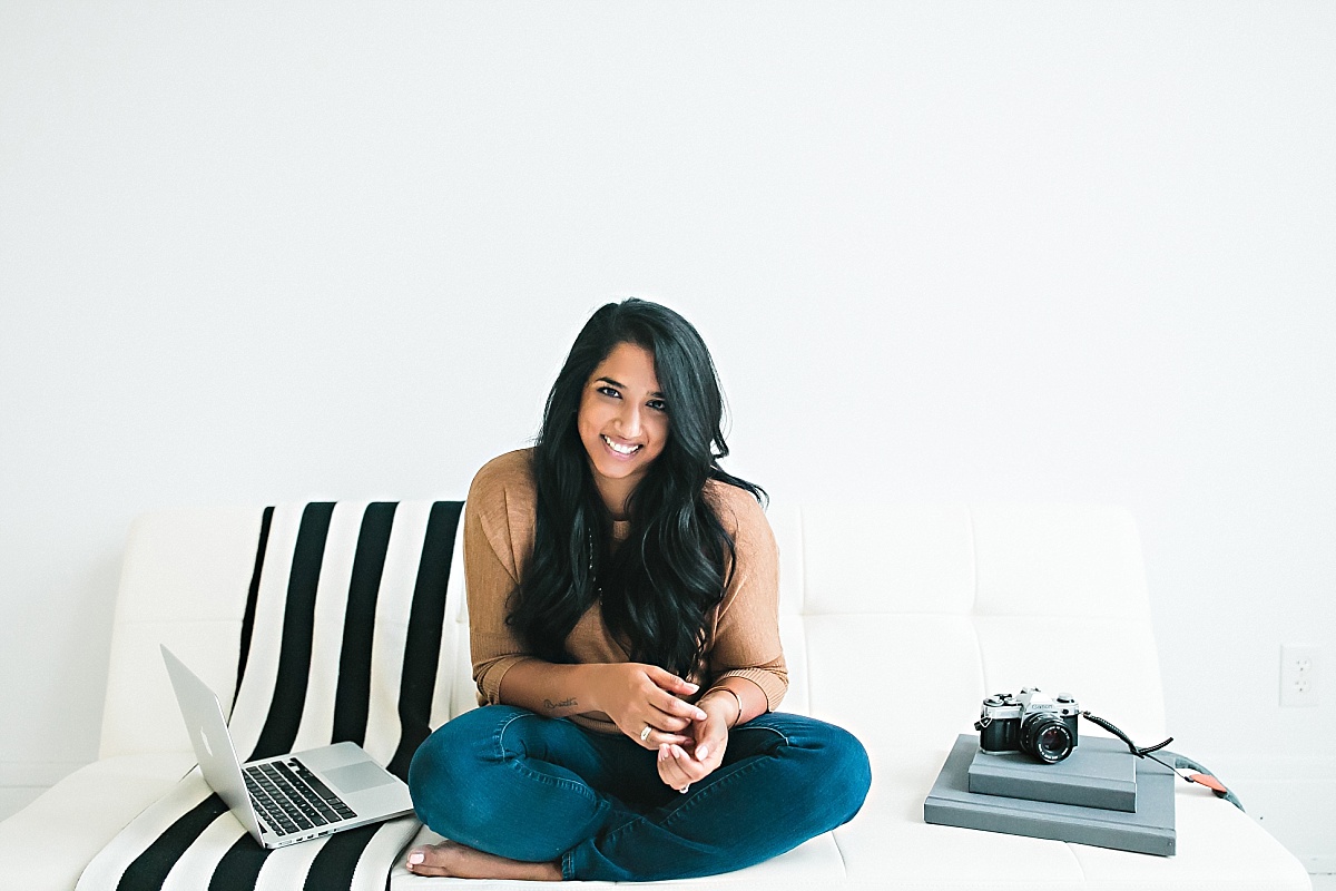 Photographer Rohana Olson of Comfort and Cashmere Images smiling at the camera while sitting on a couch next to a laptop and camera, sharing her productivity work from home tips