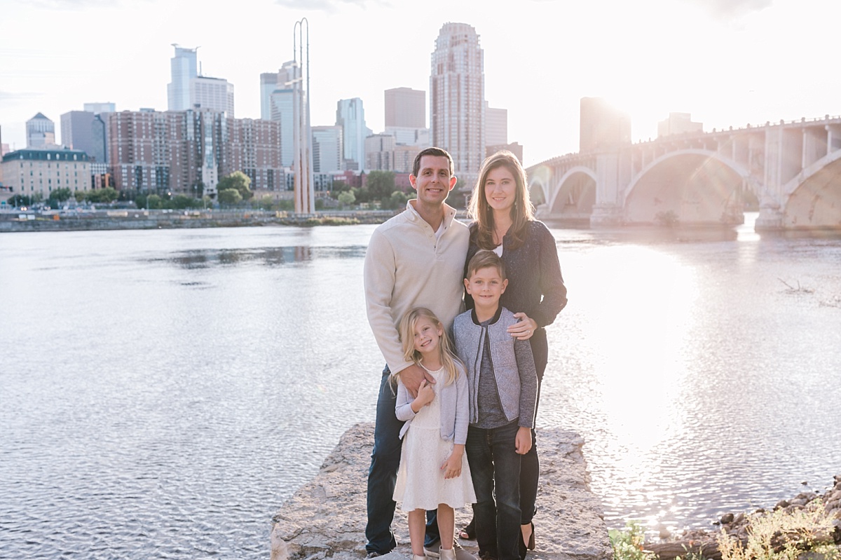 Attractive family stands in front of a river and city skyline for family photographs in Minnesota with Comfort & Cashmere Images