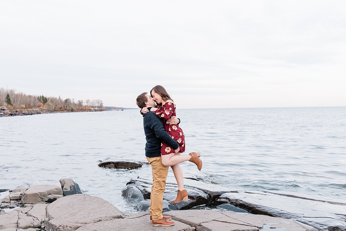 Man picks up his fiance while kissing her during a beautiful waterfront engagement photo shoot