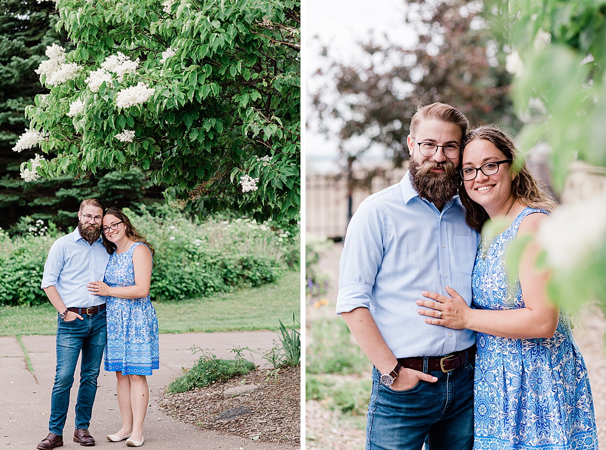 couple stands together under a blooming tree at the Rose Gardens in Leif Erickson park during their engagement session with Comfort and Cashmere images.