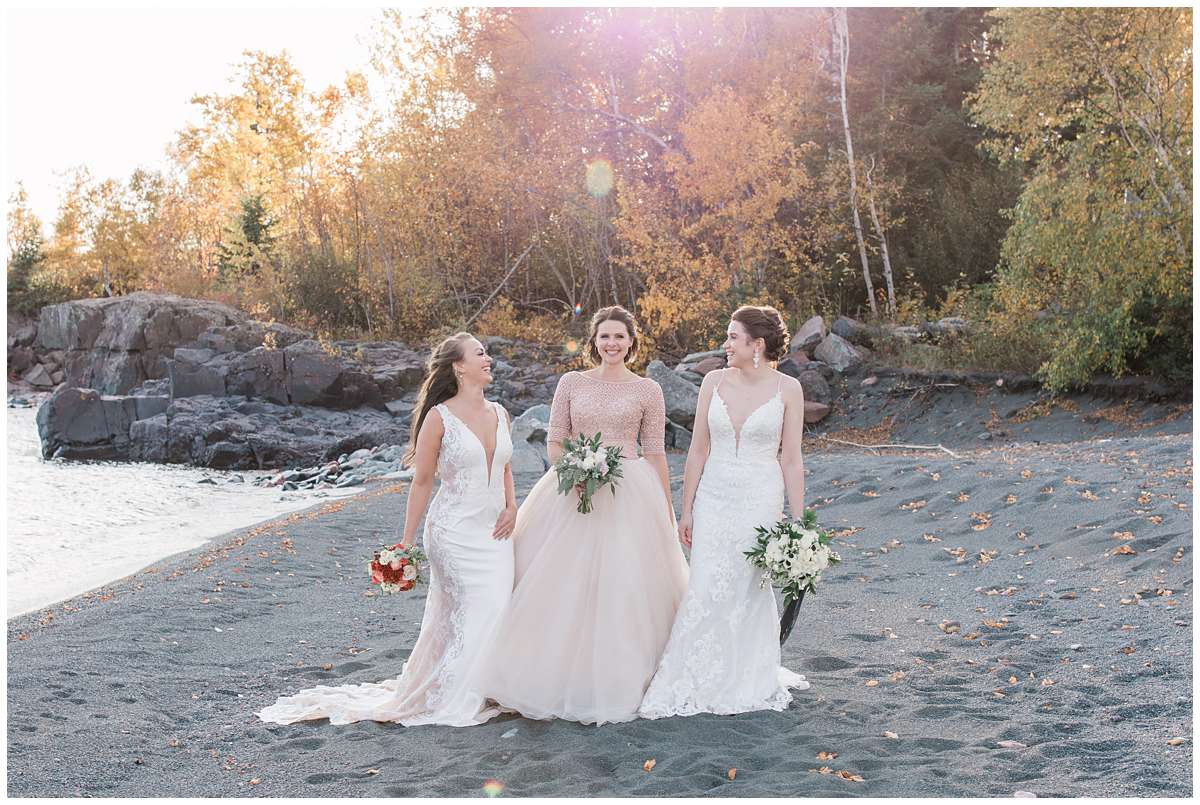 three brides wearing various styles of dresses stand on black beach in minnesota with Rohana from Comfort & Cashmere Images