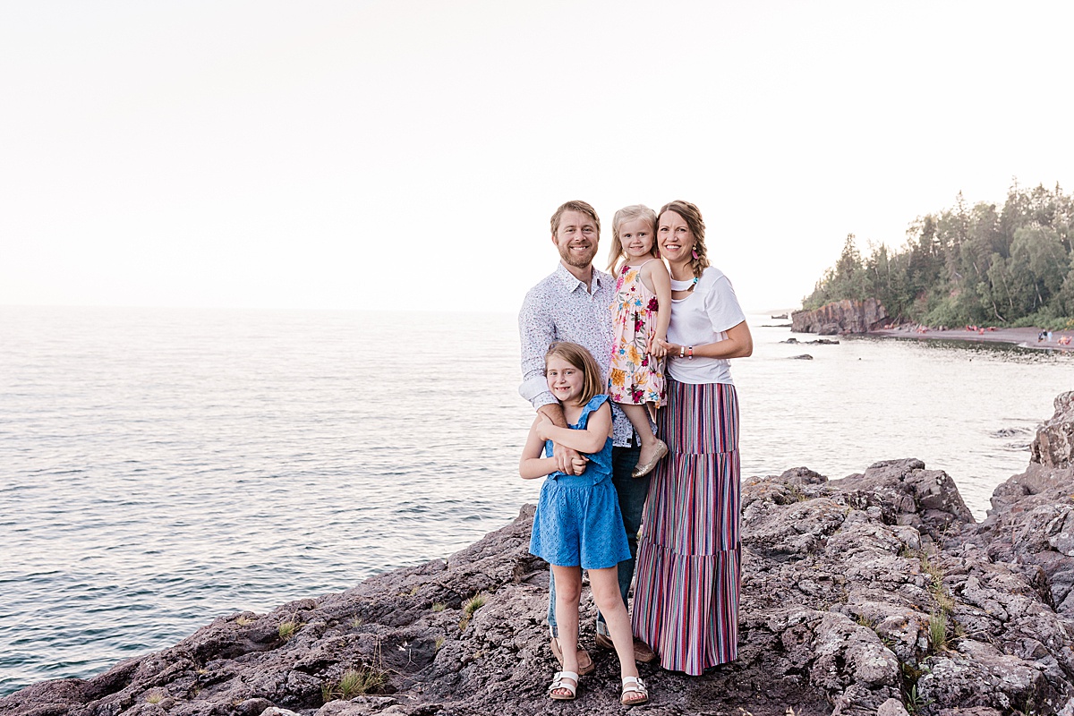 A family poses for a smiling photo on some rocks on the lakeshore of Lake Superior during a sunset family photo session