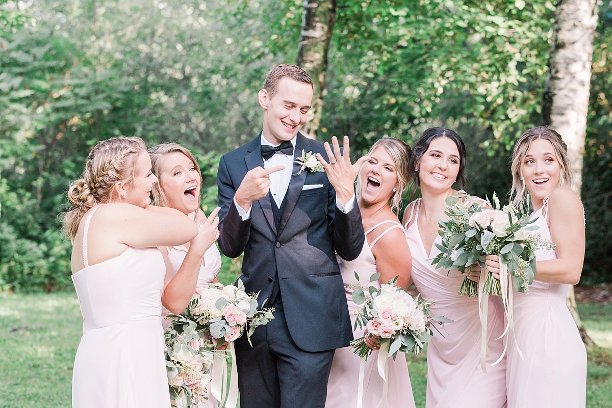 A bridal party laughs and points at the groom, holding up his ring and posing as if he is the bride.