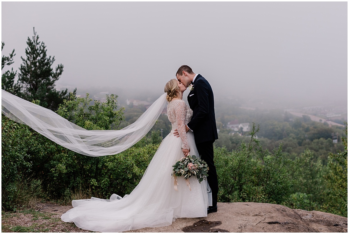 A bride and groom kiss in front of a foggy Minnesota backdrop for photos with Duluth wedding photographer Comfort & Cashmere Images.