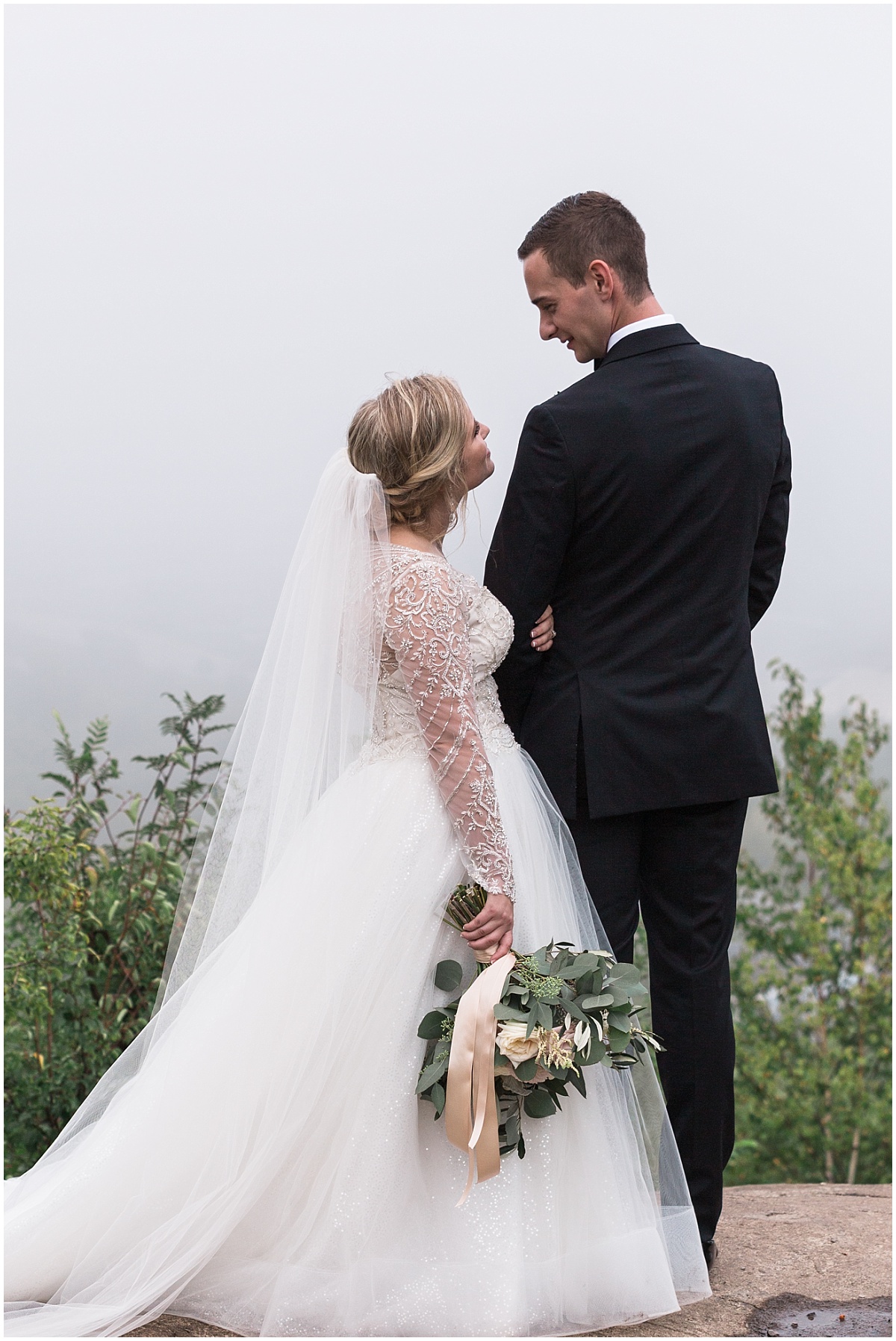 A bride looks up at her groom in front of a foggy backdrop for photos with Duluth wedding photographer Comfort & Cashmere images.