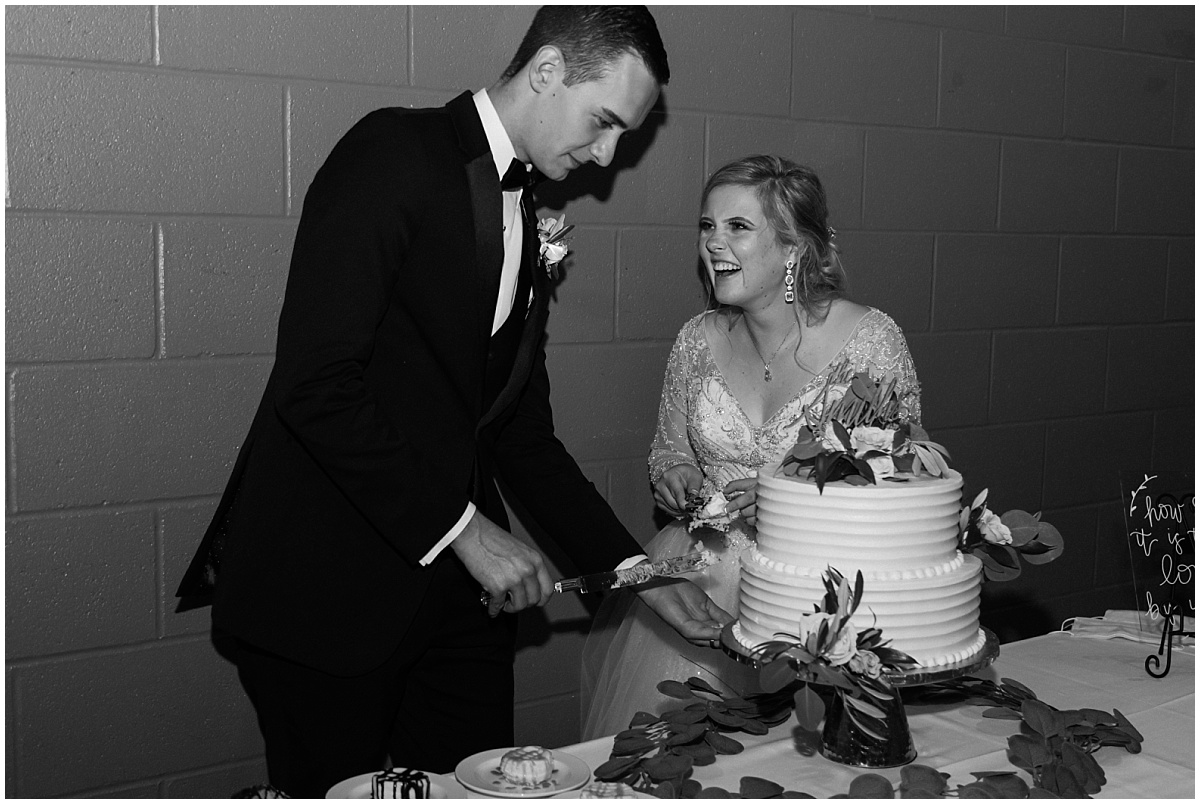 A newlywed couple smile as they cut the cake at their Clyde Iron Works wedding in Duluth, Minnesota.