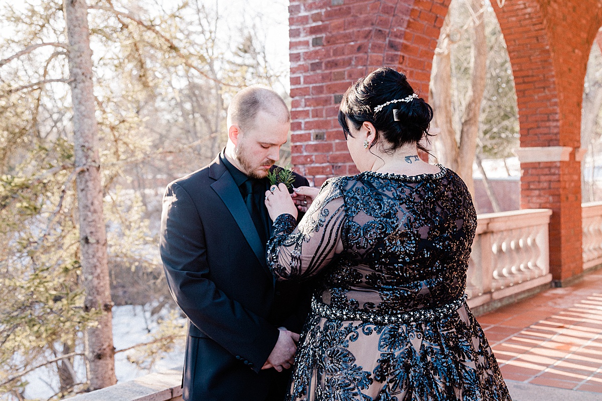 a curvy bride wearing a black gown pins on her groom's boutonniere before their Glensheen elopement ceremony 