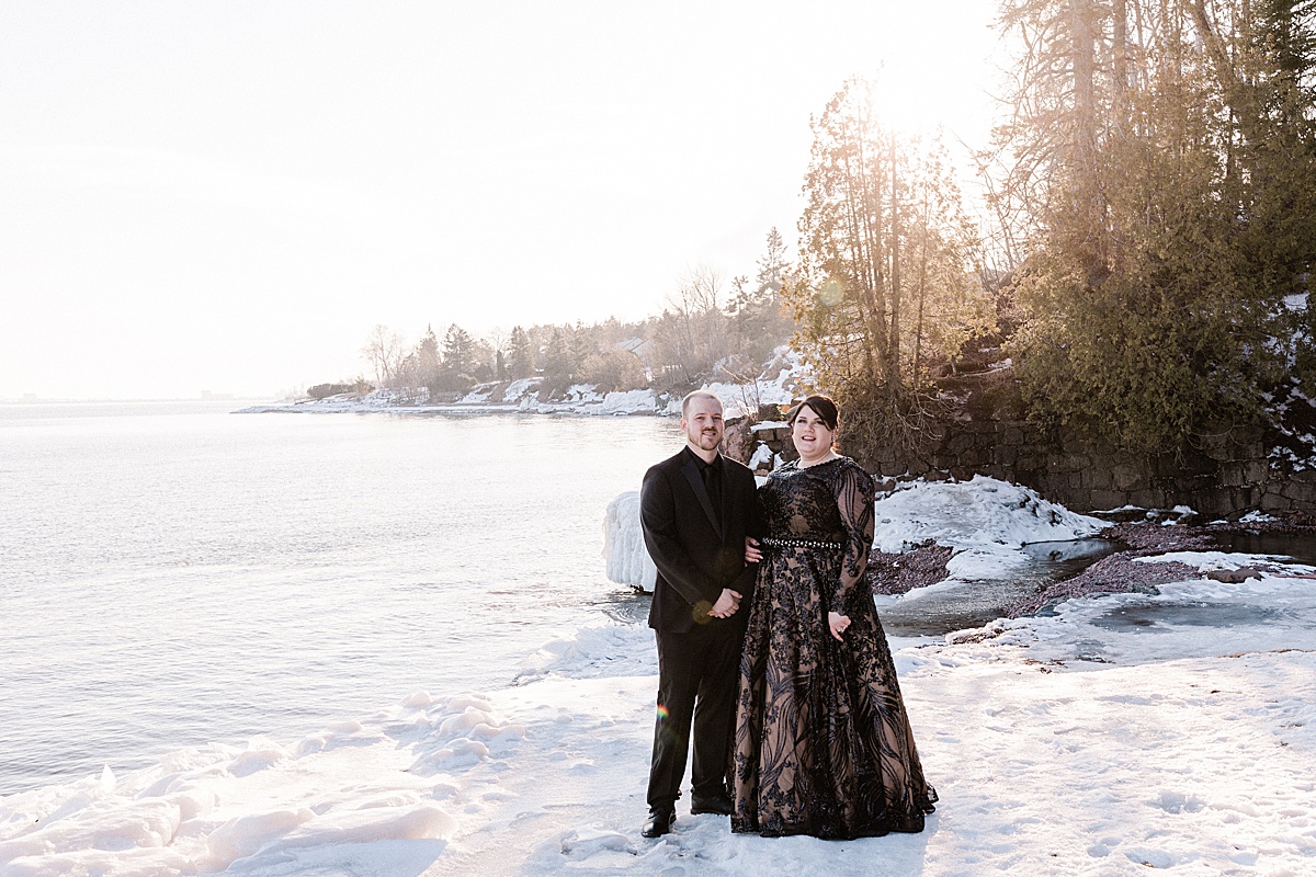 bride wearing a black dress and her groom pose on the snowy shore of frozen Lake Michigan