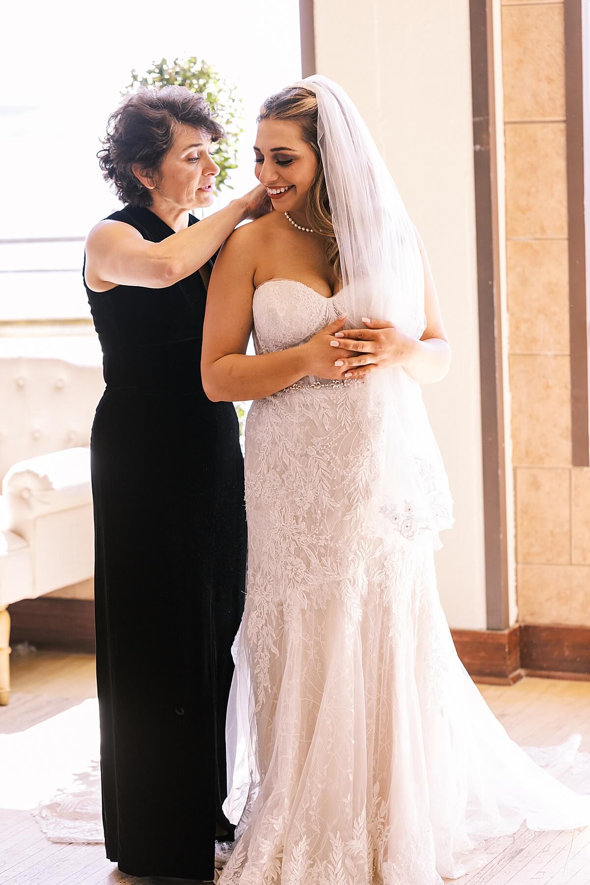 bride smiling at her mom as she finishes zipping up her wedding dress