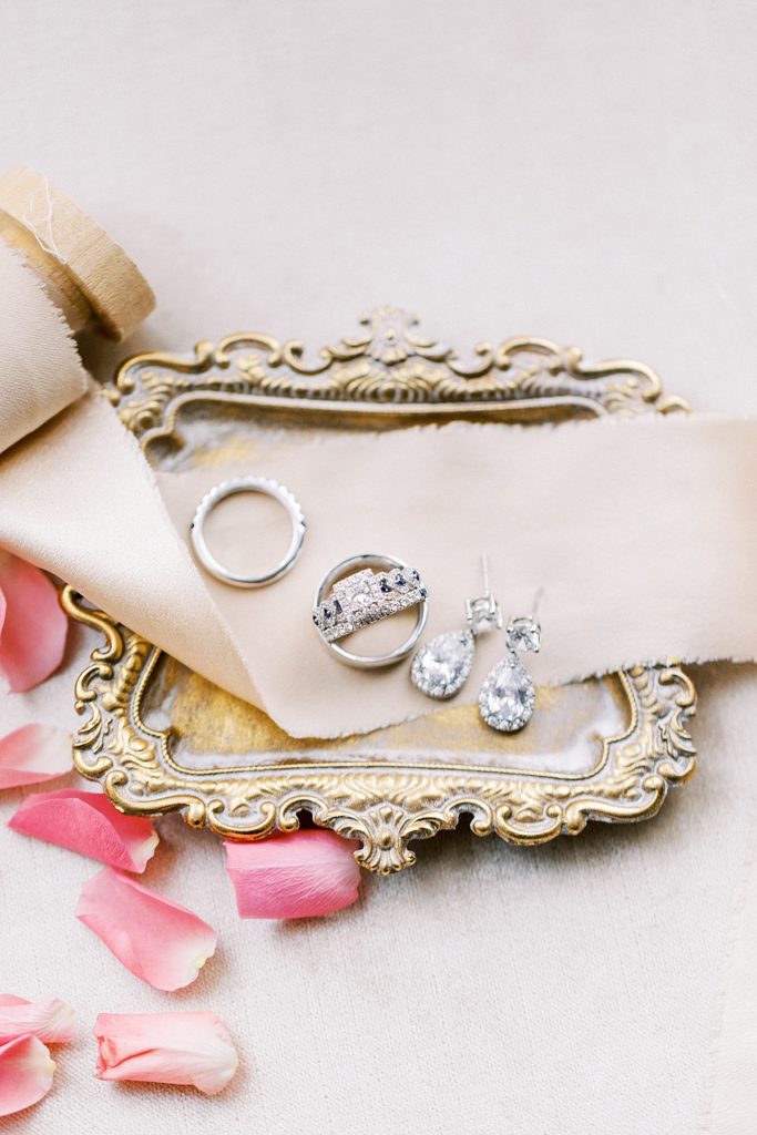 wedding rings and earrings on a dish with ribbons
