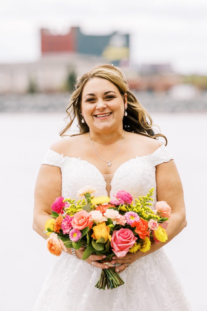 bride holding bouquet of florals with bright colors like pink, orange, cream, and peach.