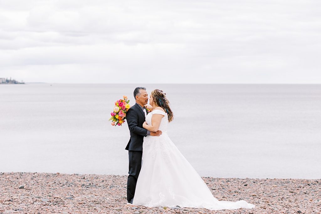 bride and groom standing on beach against lake superior