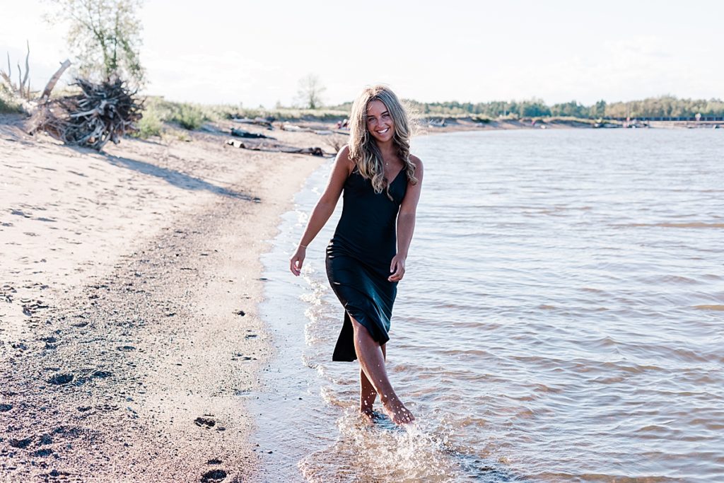 class of 2021 girl wearing black dress splashing in water at Wisconsin point 
