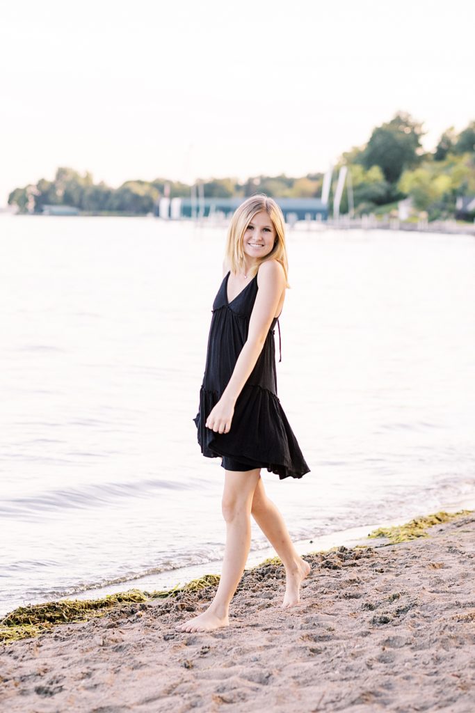 senior girl walking along wazyata beach in black dress and bare feet.